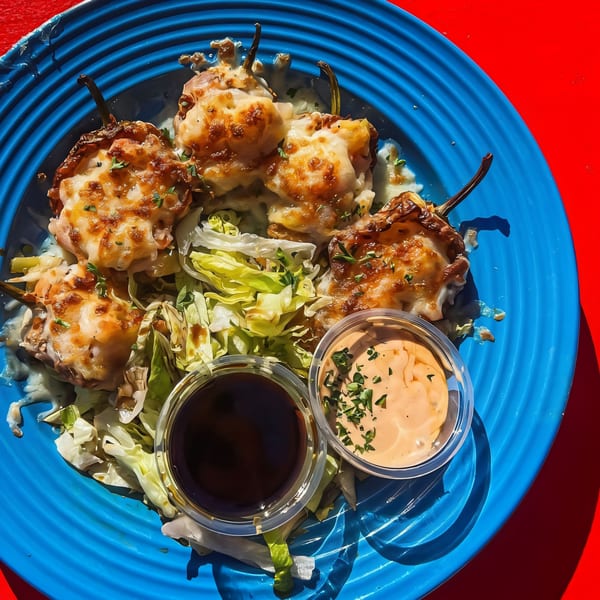 Four cheese-covered stuffed peppers on a bed of lettuce with two dipping sauces on a blue plate.
