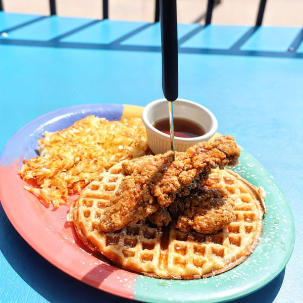 Chicken and waffles with hash browns and syrup on a colorful plate at Loco Charlies.