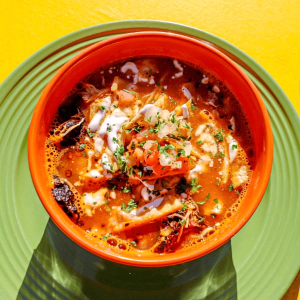 Loco Charlies' Mexican soup with pico de gallo, sour cream, and cilantro in an orange bowl.