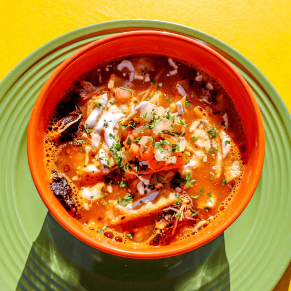 Loco Charlies' Mexican soup with pico de gallo, sour cream, and cilantro in an orange bowl.