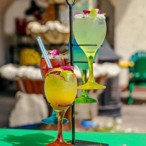 Three colorful Loco Charlies margaritas, garnished with fruit and salt, on a black metal stand.