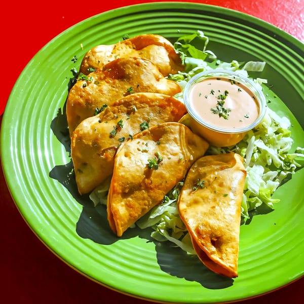Golden-brown empanadas with shredded lettuce and a side of creamy sauce on a vibrant green plate.