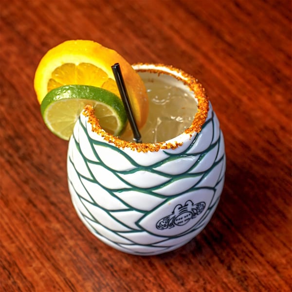 A Loco Charlies margarita in a decorative white and green cup, garnished with orange and lime slices.